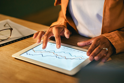 Businesswoman working on a tablet screen, analyzing graphs, doing marketing seo data research or website analytics engagement. Closeup of a business analyst using a latest finance management software