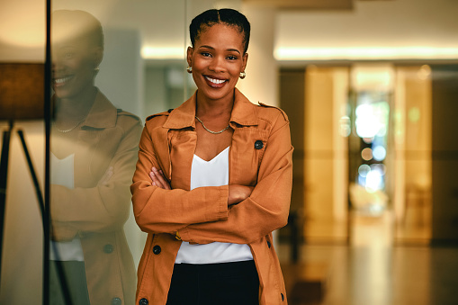 Creative, black female and business woman in leadership, standing in a modern office building. Happy startup entrepreneur hiring and welcoming new candidates and employees, smiling arms crossed.