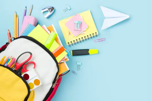 Photo of Many colorful school supplies and backpack arranged on blue background