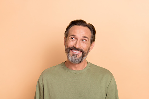 Portrait of satisfied minded man toothy smile look interested empty space isolated on beige color background.