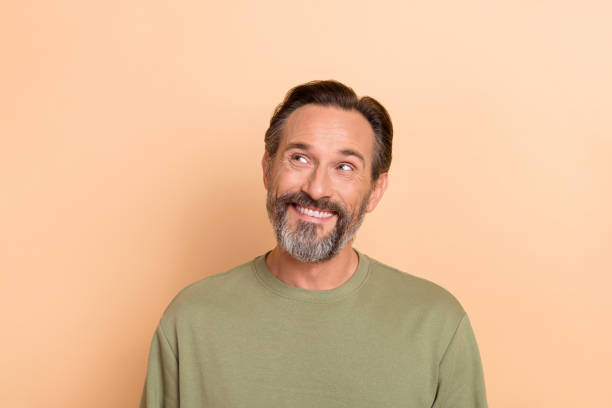 Portrait of satisfied minded man toothy smile look interested empty space isolated on beige color background stock photo