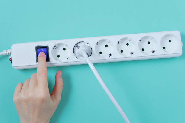 white surge protector with sockets.  hand presses the power button. turquoise background. - home addition audio imagens e fotografias de stock