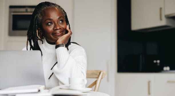 femme d’affaires mature détournant les yeux pensivement dans son bureau à domicile - african ethnicity women laptop computer photos et images de collection