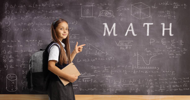 istock Child in school uniform with a backpack and book pointing at a blackboard with math formulas 1414384157