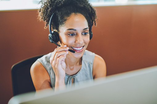 Smiling, helping and working customer support service worker with a headset and office computer. Call center worker on a online internet consulting call. Telephone operator agent giving web advice