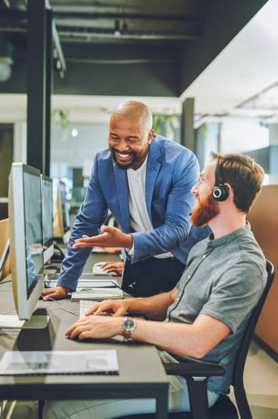 istock Manager, mentor or call center supervisor giving advice and helping agent while working on his computer and wearing headset. Teamleader assisting, teaching and training new operator sales and support 1414393945