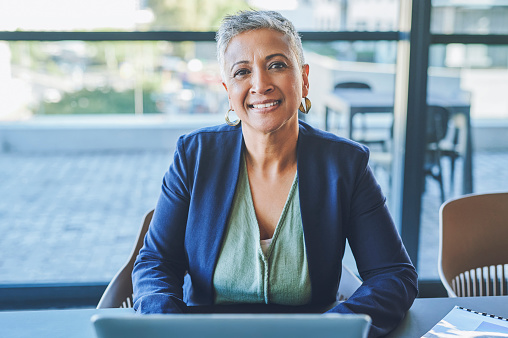 Mature woman with laptop smiling, looking happy and cheerful while waiting or listening to job candidate at an interview. Portrait of a friendly human resource manager getting ready to meet employees