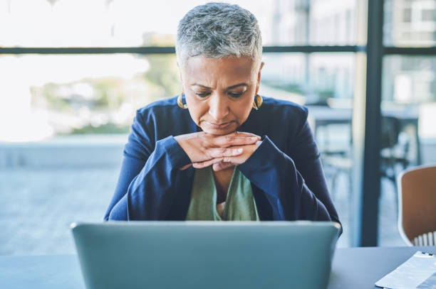 donna d'affari triste, infelice e stanca che naviga online su un laptop, legge un'e-mail con cattive notizie o soffre di burnout mentre è seduta in un ufficio. capo femminile maturo che affronta un problema di lavoro - senior women depression sadness women foto e immagini stock