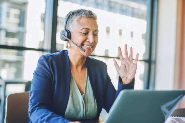 istock Call center agent helping clients, greeting and networking in a virtual meeting with laptop online in office at work. Mature customer service worker and helpdesk operator in video conference 1414393982
