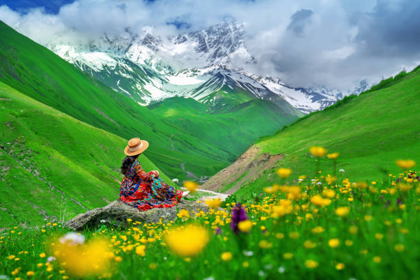 Tourist sitting on the rock at green pasture against highest georgian mountain Shkhara near Ushguli in Georgia. stock photo