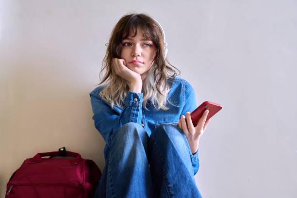 istock Sad young female student with backpack smartphone sitting on the floor 1414395389