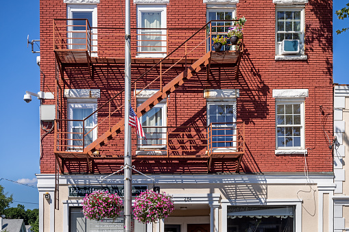 Beacon, Dutchess County, New York, NY, USA - July 3 2022: Fire escape on a brown stone building with surveillance cameras, flowers and a American flag