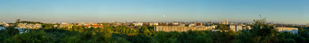 Large panoramic view of Munich from northeast to southeast during a sunny summer evening with the moon rising over the horizon