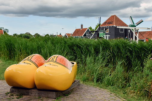 Two yellow wooden clogs, in the background, views of the village of Zaanse Schans, in the Netherlands.