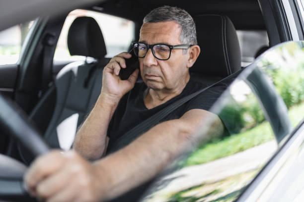 istock Senior in his 70s driving a car and using his mobile phone 1414402128