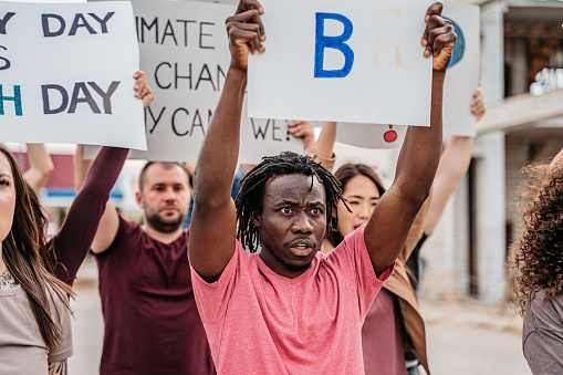 Group of people protesting against climate change on the street. Holding placards and posters. Close-up of a young black man.