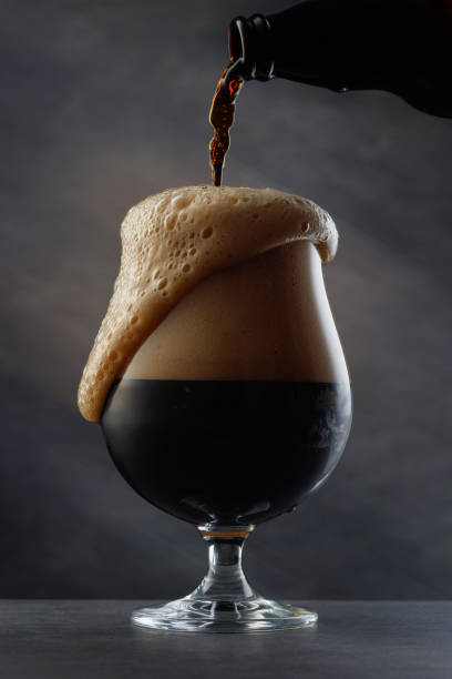 Detail of dark beer with overflowing foam head. Stream of dark stout pours into a beer glass. bitter stock pictures, royalty-free photos & images