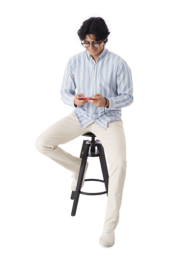 A happy male student sitting and using a mobile phone with a smile.