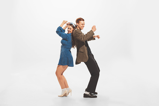 Portrait of young beautiful couple, stylish man and woman dancing at the retro party isolated over white studio background. Concept of retro fashion, style, youth culture, emotions, beauty, ad