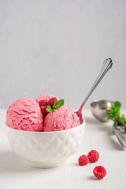 istock Scoops of raspberry ice cream with red berries and mint leaf served in bowl with spoon on white wooden table 1414410897