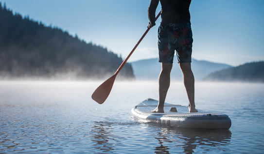 Low section of unrecognizable man riding a paddle board in a mountain lake.