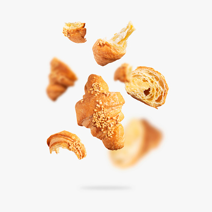 Flying whole and broken fresh croissant with butter cream isolated on light gray background. Creative bakery food background, croissant sprinkled with nuts. Sweet pastry, bun, dessert, confectionery.