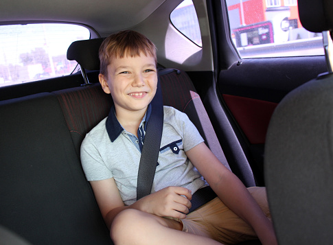 The boy is wearing a seat belt sitting in the back seat of the car. Close-up portrait.