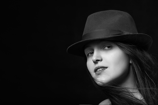 woman with hat and blowing hair on black background with copy space looking at camera monochrome