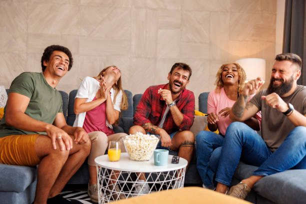 Friends laughing while watching TV at home stock photo