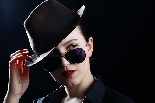 woman with hat and sunglasses on black background with copy space