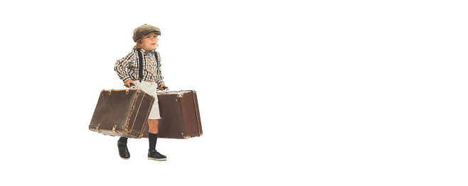 Portrait of cute little boy, happy kid going with retro suitcase isolated on white studio background. Retro vintage style concept. Holidays, vacation, trip. Concept of child emotions, facial expression