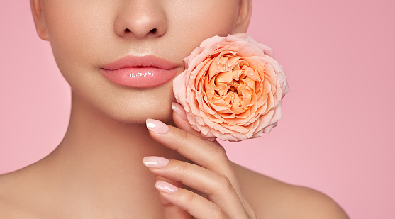 Beautiful model with a rose. Perfect woman face makeup close up. Lipstick. Beautiful nails. Nice smile. Perfect skin
