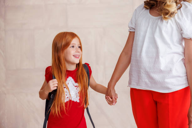 Mother holding hands with her little daughter while taking her to school - first grade student and first day of school