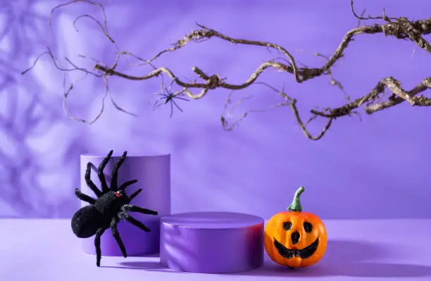 Photo of Halloween holiday concept.Podiums or pedestals for products display. Spiders and pumpkin over purple background.