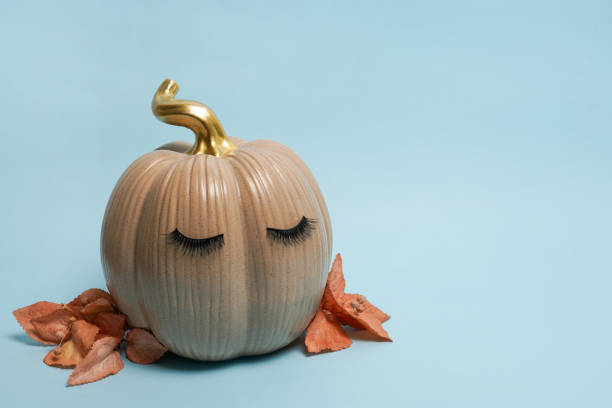 istock Pumpkin with false eyelashes and autumn leaves on blue background. Autumn, fall, halloween concept. copy space 1414422576