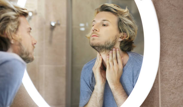 istock young man looking in the mirror,combing his hair,looking at problems on face 1414424888