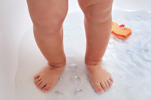 Toddler baby legs is standing on a non-slip mat in the bathtub. Child boy foots washes on the anti slip carpet in the bathroom. Kid age one year