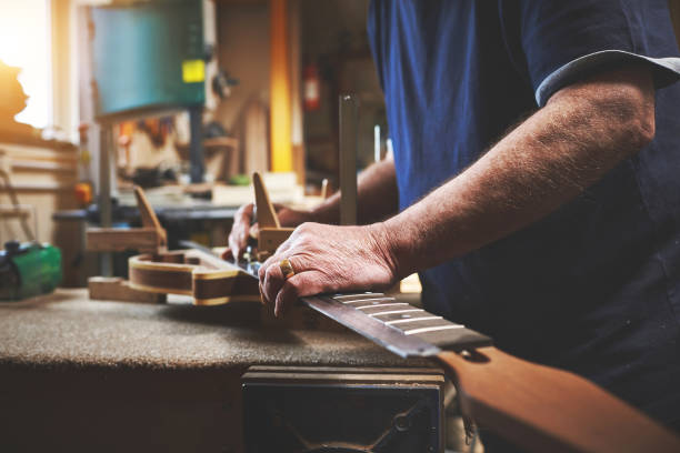 primer plano de manos de hombre reparando, arreglando y construyendo una guitarra en el taller de servicio de luthiers. hombre profesional de pie, medición y mantenimiento de instrumentos musicales en el banco de trabajo en su garaje. - fabricante de instrumentos fotografías e imágenes de stock