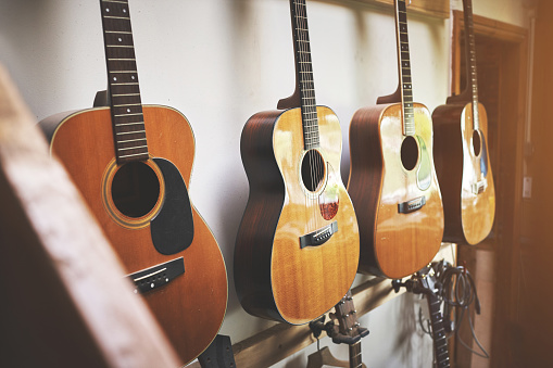 Group of classic musical guitar instruments on display in a music shop. Classical vintage acoustic guitars of a  instrument made from art wood hanging on a rack in a new indoor local store.