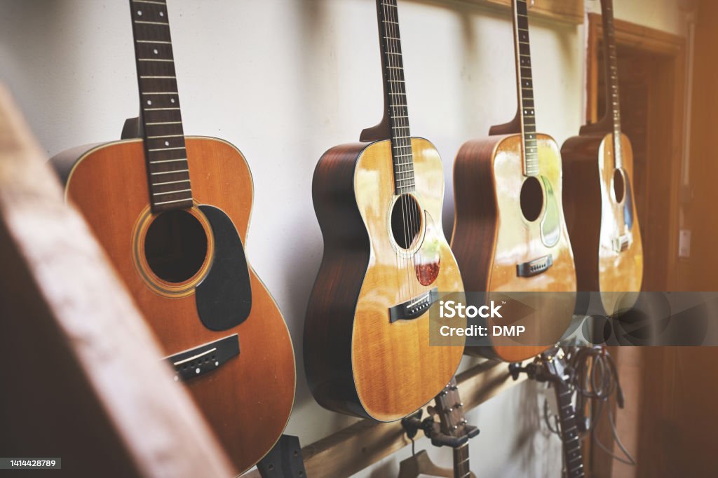 Group of classic musical guitar instruments on display in a music shop. Classical vintage acoustic guitars or  instruments made from art wood hanging on a rack in a new indoor local store. Group of classic musical guitar instruments on display in a music shop. Classical vintage acoustic guitars of a  instrument made from art wood hanging on a rack in a new indoor local store. Guitar Stock Photo
