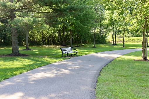 The empty park bench on the pathway in the park..