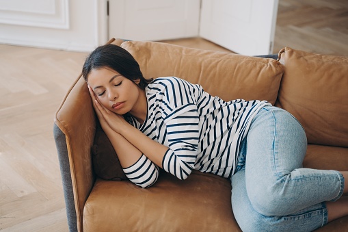 Tired female lying on sofa takes day nap rests after sleepless night at home. Woman housewife sleeping on cozy couch, relaxing after house working in living room. Fatigue, lazy time concept.