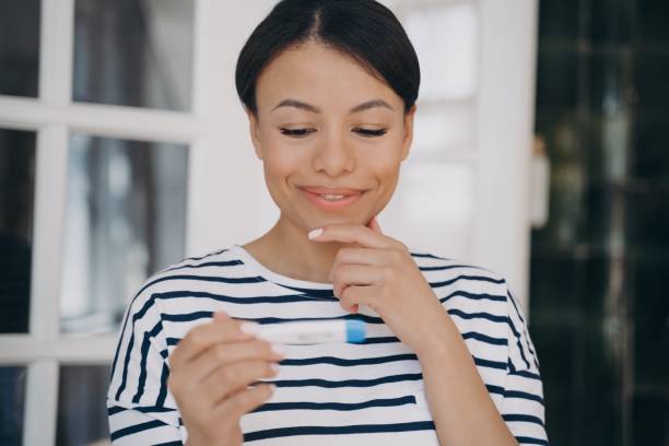 charmante jeune femme regardant le test de grossesse et souriant. femme satisfaite tenant un test d’ovulation. - kit mains libres photos et images de collection