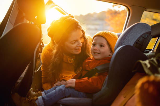 Mother fastening her son safely in a car seat stock photo