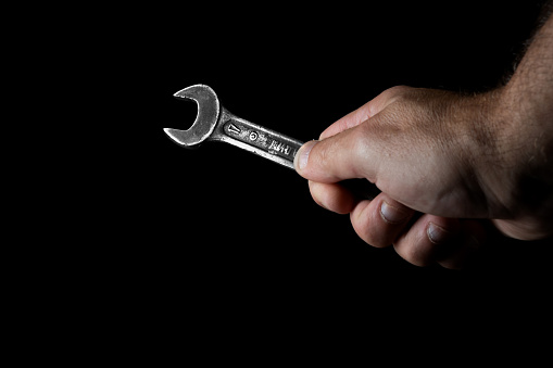 Old wrench in hand on a black background. High quality photo