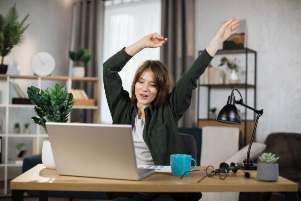 istock Excited businesswoman sitting at table with modern laptop and keeping arms raised 1414440607