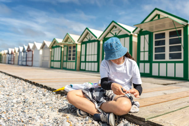 girl playing with pebbles in front of colorful wooden beach huts at beach girl playing with pebbles in front of colorful wooden beach huts at beach in Cayeux-sur-Mer, France normandy photos stock pictures, royalty-free photos & images