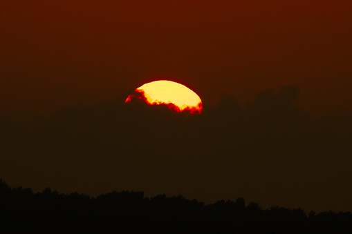 A beautiful sunset, clouds hiding the sun with shadow of trees, shot with telephoto lens