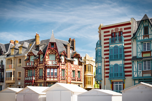 white traditional wooden beach huts in front of multi-colored facades of historic houses alongside the beach promenade in Mers-Les-Bains at the atlantic coast