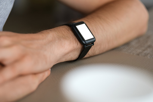 Close up shot of a man  wearing smart watch with white screen, copy space, cup of coffee out of focus bottom right.